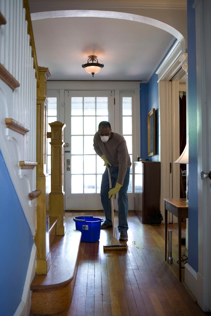 A person wearing purple rubber gloves is cleaning a window with a cloth, with a view of greenery outside.
